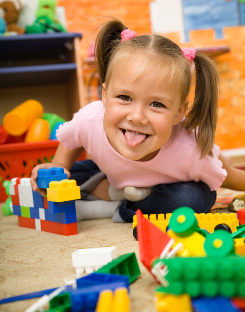 Little,Girl,Is,Showing,Tongue,While,Playing,With,Building,Bricks