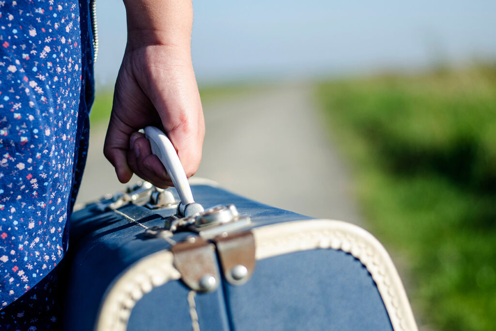 Young,Refugee,Girl,Carrying,Her,Old,Suitcase,While,Walking,On