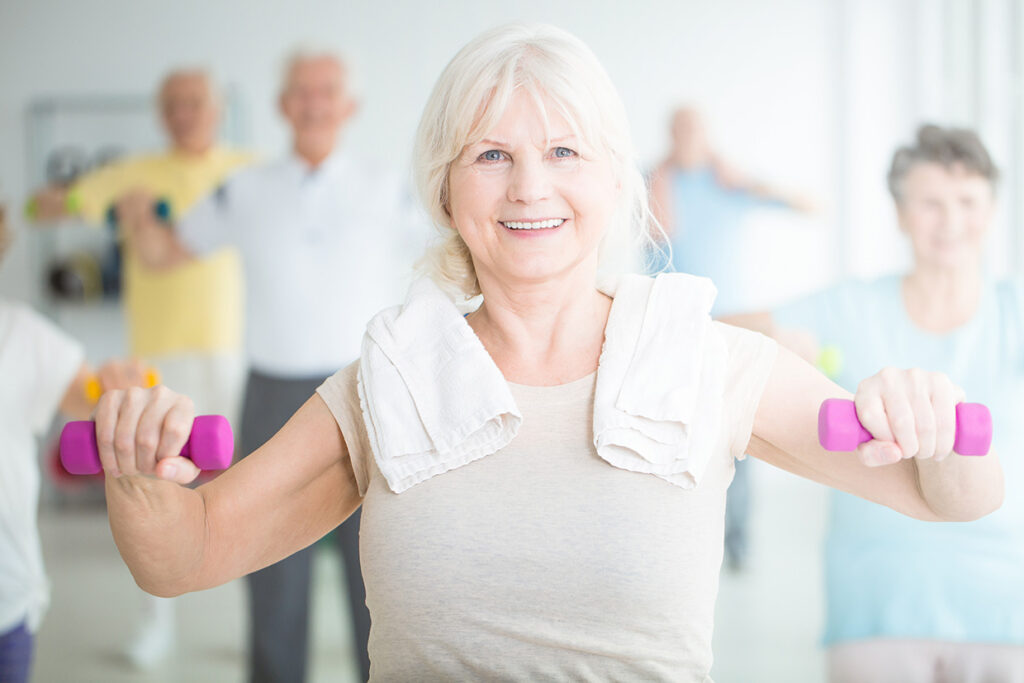 Smiling,Elderly,Woman,Exercising,With,Pink,Dumbbells,In,Fitness,Center